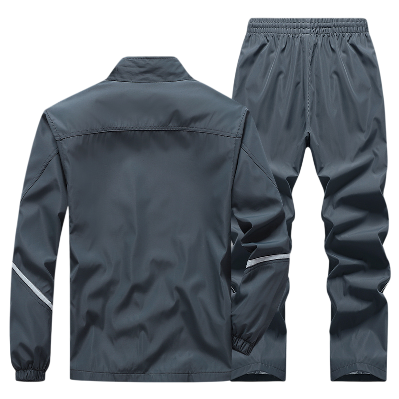 Dres komplet męski dwuczęściowy Arkadya Outlet: szara bluza na zamek z odblaskowymi paskami i długimi rękawami oraz spodnie z elastycznym pasem, luźnym krojem i lekkiego, błyszczącego materiału.