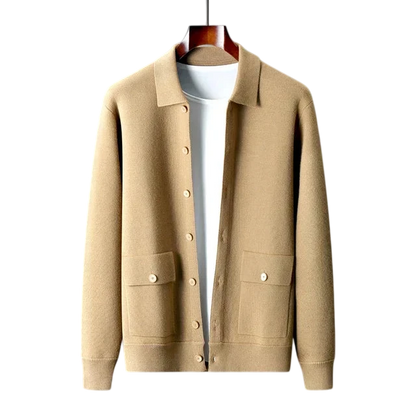 Kardigan męski zapinany na guziki z kołnierzem i kieszeniami Arkadya Outlet w beżowym kolorze prezentowany jest na wieszaku na białej koszuli, na tle gładkiej szarej ściany.