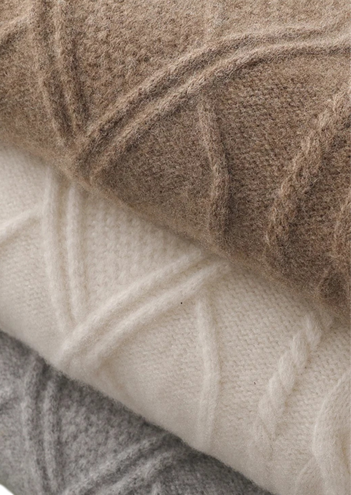 Zbliżenie na trzy złożone swetry męskie Arkadya Outlet Sweter dekolt okrągły warkoczowy w kolorze beżowym, białym i szarym z teksturowanym krzyżowym wzorem - idealne do klasycznej całorocznej kolekcji męskiej.