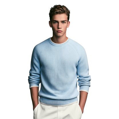 Młody mężczyzna z krótkimi brązowymi włosami modeluje Arkadya Outlet Sweter męski dekolt okrągły prążkowana dzianina standardowy krój z białymi spodniami, stojąc na jednolitym białym tle, ręce w kieszeniach.