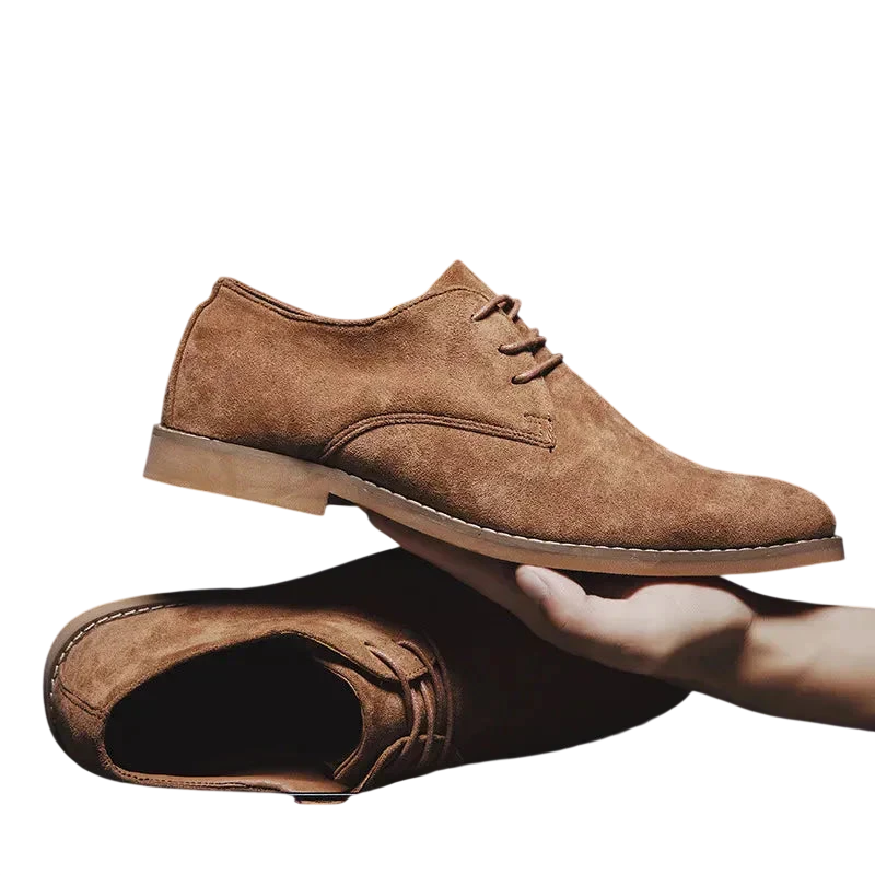 Ręka trzyma elegancki Arkadya Outlet Buty Biznesowe Męskie Płaski Obcas Zamknięty Nosek nad pasującym butem leżącym płasko na białym tle.