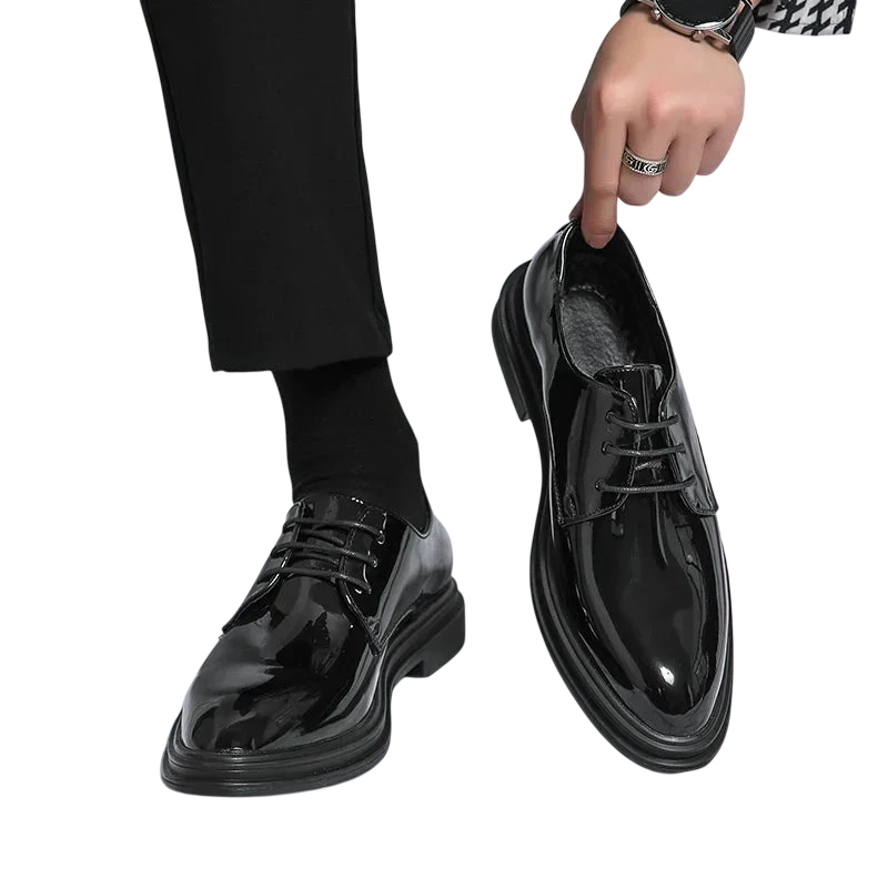 Osoba ubrana w Buty Wizytowe Męskie Sznurowane Oxfordy Spiczasty Nosek by Arkadya Outlet i czarne spodnie trzyma pasujące buty na białym tle.