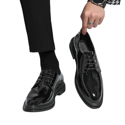 Osoba ubrana w Buty Wizytowe Męskie Sznurowane Oxfordy Spiczasty Nosek by Arkadya Outlet i czarne spodnie trzyma pasujące buty na białym tle.