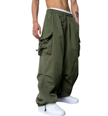 Osoba modeluje Męskie Spodnie cargo Arkadya Outlet - luźne oliwkowozielone spodnie cargo z szerokimi nogawkami i wieloma kieszeniami - w połączeniu z białymi trampkami. Ich tors jest nagi, odsłaniając tatuaż na lewym przedramieniu, na prostym tle.