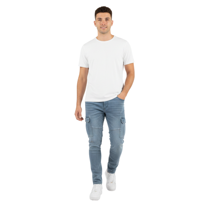 Młody mężczyzna z krótkimi brązowymi włosami idzie w kierunku kamery, ubrany w zwykłą białą koszulkę, białe trampki i Arkadya Outlet Spodnie cargo męskie wąski krój codzienne spodnie kieszeniowe, z jedną ręką w kieszeni na białym tle.