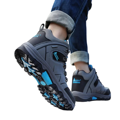 Mężczyzna w Arkadia Outlet Męskie buty wodoodporna konstrukcja ergonomiczna podeszwa stoi na skale, stopa uniesiona, aby pokazać ergonomiczny bieżnik. Podwinięte dżinsy i rozmyte drzewa podkreślają te idealne buty do codziennego użytku.