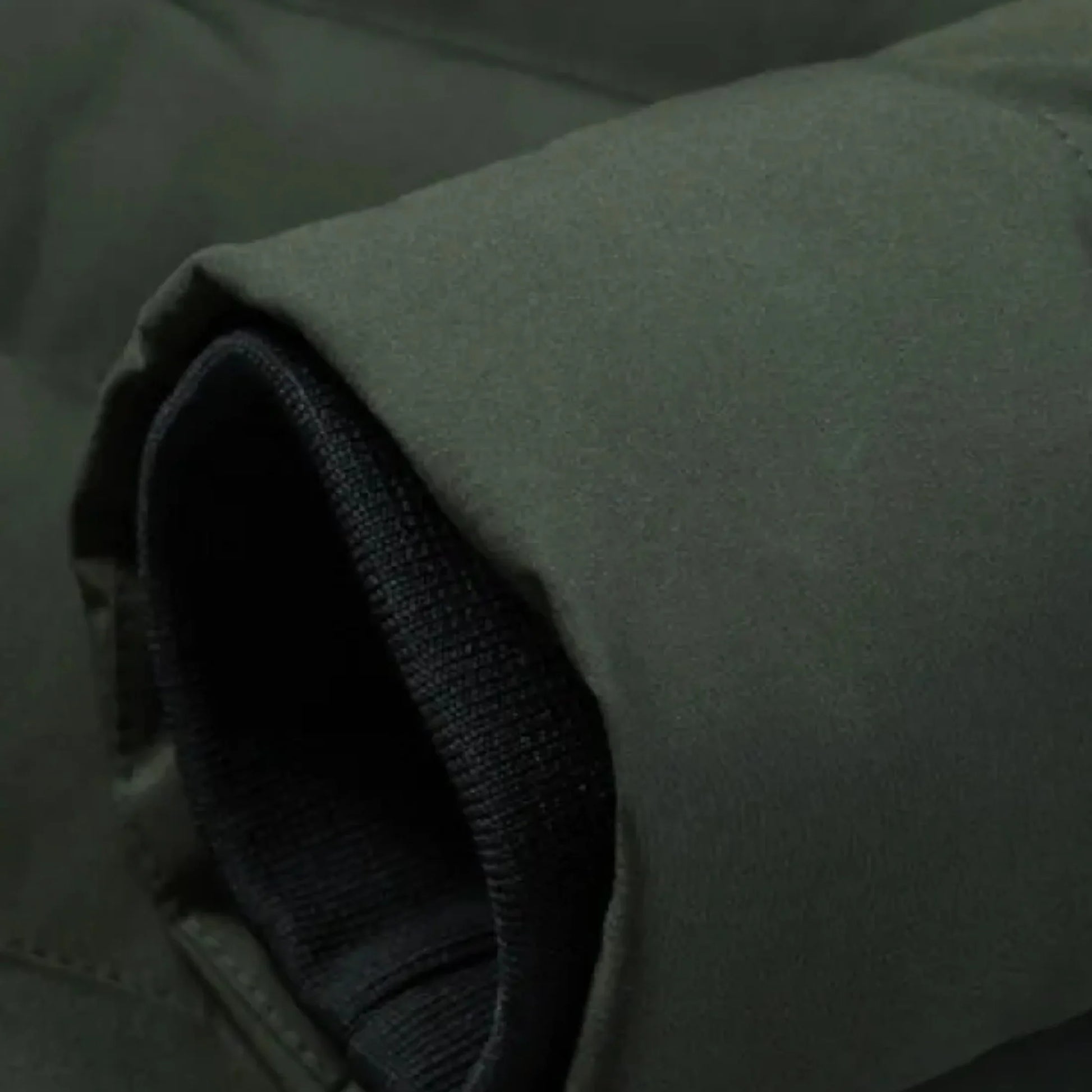 Zbliżenie na rękaw kurtki Arkadya Outlet Męska kurtka grzewcza zimowa odzież wierzchnia z ociepleniem, ukazujące czarny prążkowany mankiet z dzianiny wewnątrz ciemnozielonego materiału zewnętrznego z widocznymi materiałami i przeszyciami.