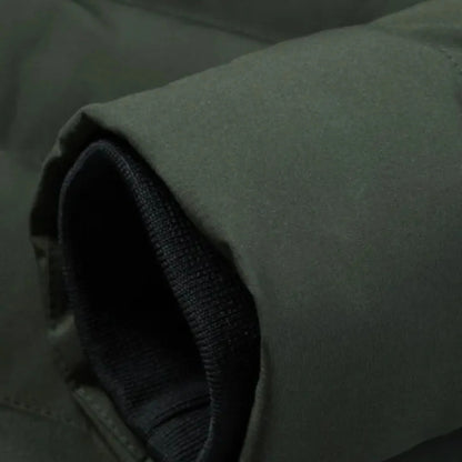 Zbliżenie na rękaw kurtki Arkadya Outlet Męska kurtka grzewcza zimowa odzież wierzchnia z ociepleniem, ukazujące czarny prążkowany mankiet z dzianiny wewnątrz ciemnozielonego materiału zewnętrznego z widocznymi materiałami i przeszyciami.