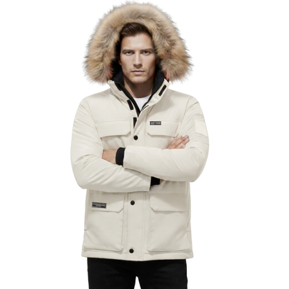 Mężczyzna stoi ze skrzyżowanymi ramionami, ubrany w Kurtkę Parka Męska Ocieplana z Kapturem na Zimę marki Arkadya Outlet, z kapturem obszytym futrem, wieloma kieszeniami i czarnymi akcentami.