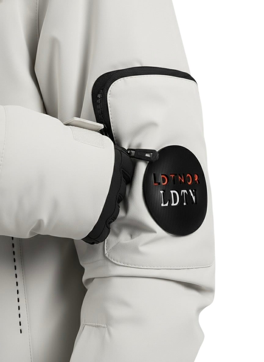 Zbliżenie na rękaw marki Arkadya Outlet Kurtka Zewnętrzna Męska Wodoodporna przedstawia czarną kieszeń zapinaną na zamek błyskawiczny oraz okrągłą czarną naszywkę z biało-czerwonym napisem LDTNOR LDTN. Częściowo widoczna jest dłoń w rękawiczce.