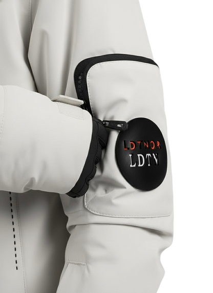 Zbliżenie na rękaw marki Arkadya Outlet Kurtka Zewnętrzna Męska Wodoodporna przedstawia czarną kieszeń zapinaną na zamek błyskawiczny oraz okrągłą czarną naszywkę z biało-czerwonym napisem LDTNOR LDTN. Częściowo widoczna jest dłoń w rękawiczce.