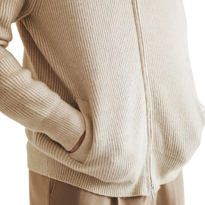 Osoba ubrana w kardigan Arkadya Outlet Męski, beżowy prążkowany sweter zapinany na zamek o dopasowanym kroju, z rękami w kieszeniach, w połączeniu z jasnobrązowymi spodniami.