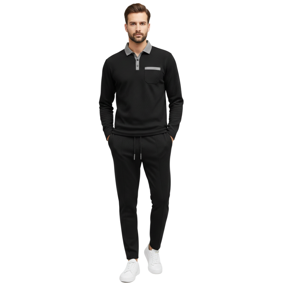 Mężczyzna z krótkimi włosami i brodą modeluje Arkadya Outlet komplet dresowy męski dwuczęściowy długi rękaw użytkowy zestaw: czarna koszula z kołnierzykiem z szarym akcentem, dopasowane czarne spodnie i białe trampki, stojąc na białym tle.