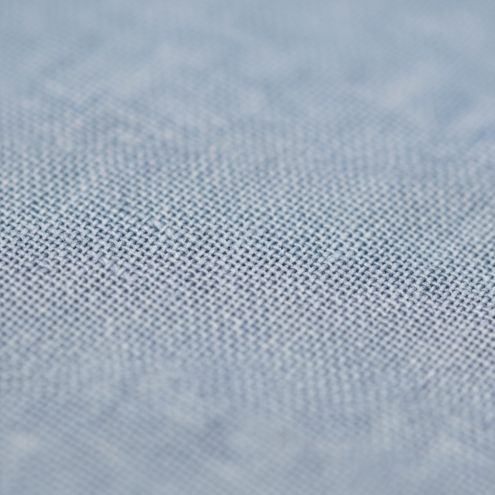 Zbliżenie jasnoniebieskiej teksturowanej tkaniny o subtelnym splocie, prezentowanej w Komplet Dwuczęściowy Męski Spodnie Robocze I Górna Część by Arkadya Outlet, podkreślającej drobne nitki i miękkie, rozmyte tło.