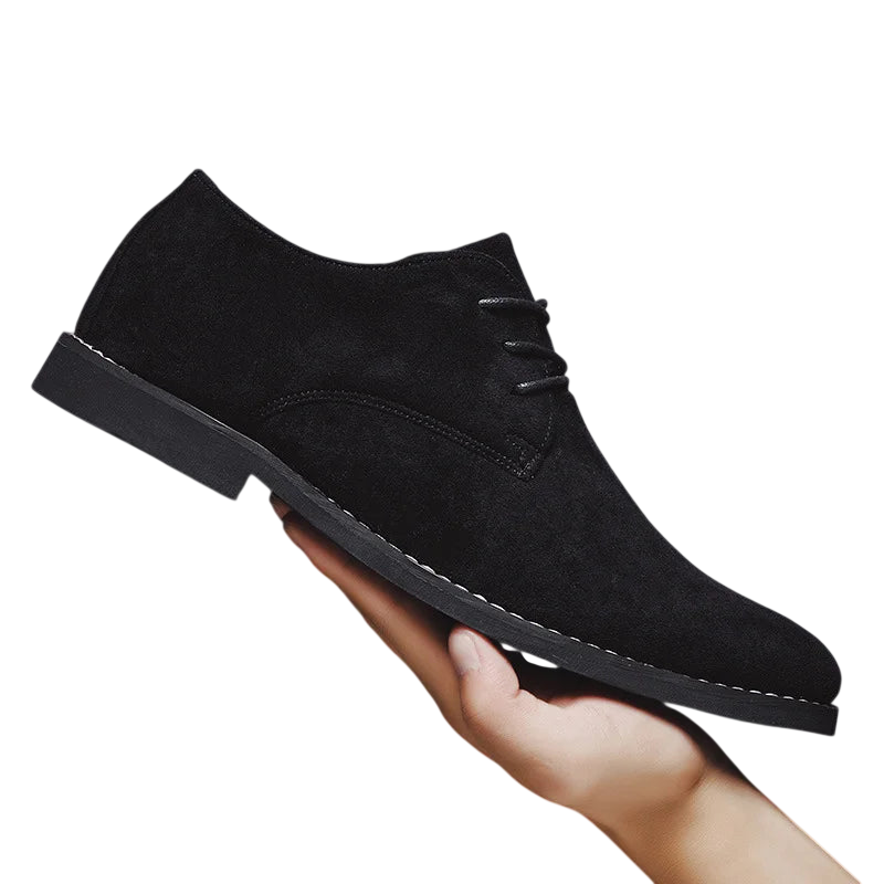 Osoba trzyma czarne Arkadya Outlet Buty Biznesowe Męskie Płaski Obcas Zamknięty Nosek z białymi przeszyciami i płaską czarną podeszwą na białym tle.