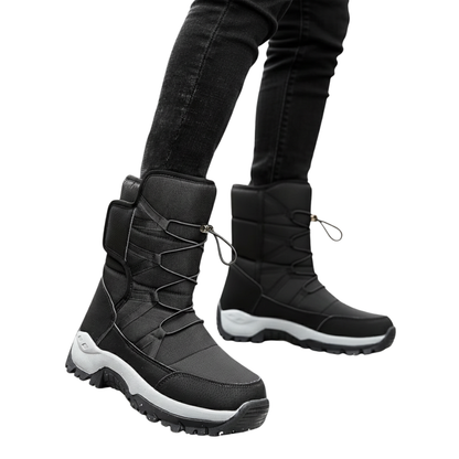 Osoba nosi czarne Buty Śniegowe Męskie Wodoodporna Zimowa Konstrukcja Zewnętrzna od Arkadya Outlet z grubymi podeszwami i sznurowadłami, w połączeniu z czarnymi jeansami skinny. Białe tło podkreśla te stylowe buty zimowe.