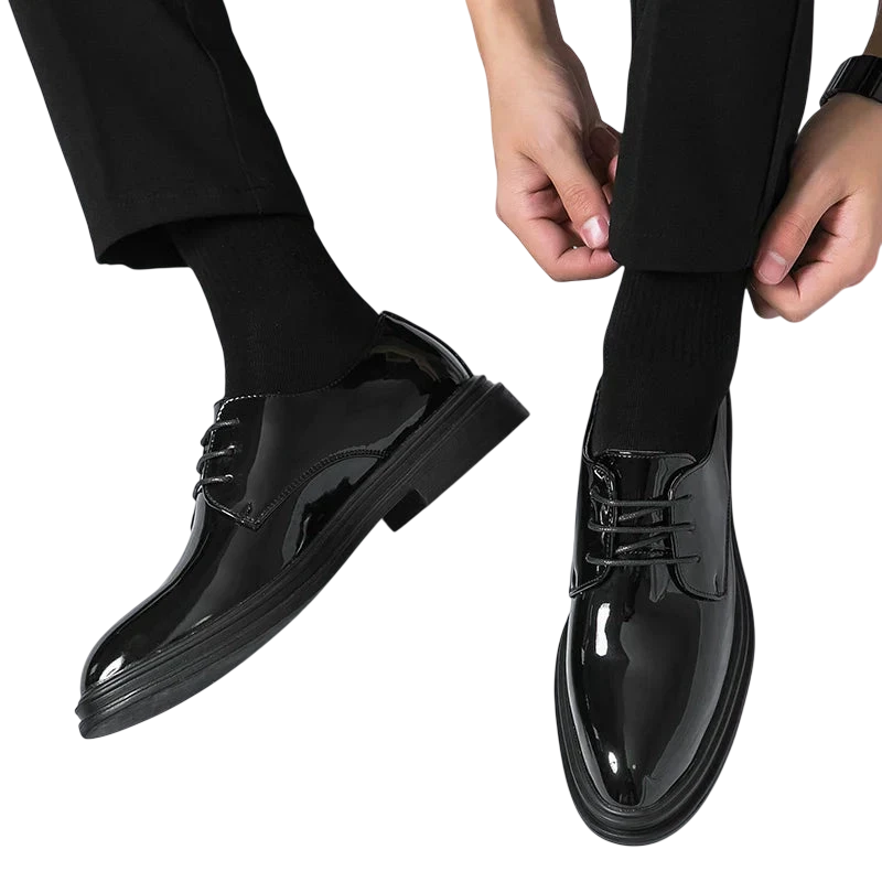 Osoba ubrana w Arkadya Outlet Buty Wizytowe Męskie Sznurowane Oxfordy Spiczasty Nosek, czarne skarpetki i czarne spodnie ręcznie reguluje mankiet spodni na białym tle.