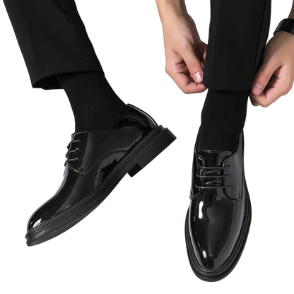 Osoba ubrana w Arkadya Outlet Buty Wizytowe Męskie Sznurowane Oxfordy Spiczasty Nosek, czarne skarpetki i czarne spodnie ręcznie reguluje mankiet spodni na białym tle.