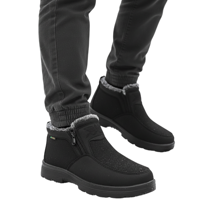 Osoba w ciemnych spodniach stoi na zaśnieżonej ziemi w lesie, ubrana w Arkadya Outlet Męskie buty wodoodporne antypoślizgowe zimowe obuwie; w tle widoczne ośnieżone drzewa.