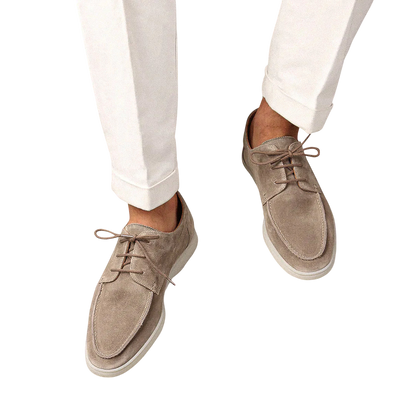 Osoba nosząca Arkadya Outlet Buty Żeglarskie Męskie Sznurowane Niskie Gumowa Podeszwa w kolorze jasnobeżowym z białymi spodniami, pokazana z góry na jednolitym jasnym tle.