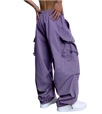 Model stoi bokiem w spodniach cargo Arkadya Outlet Męskie Spodnie z szerokimi nogawkami i wieloma kieszeniami, w połączeniu z białymi sneakersami. Spodnie są luźne i fioletowe; tors modela jest nagi, ręce spoczywają na talii na jednolitym tle.