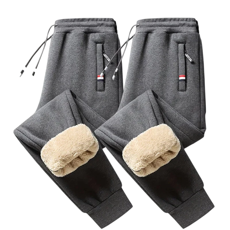 Dwie pary Arkadya Outlet Spodnie Termiczne Męskie Elastyczny Pas Z Regulacją W Talii w kolorze ciemnoszarym są pokazane na jasnej powierzchni, z zewnętrznymi kieszeniami, sznurkami i beżową polarową podszewką - idealne na chłodne dni.