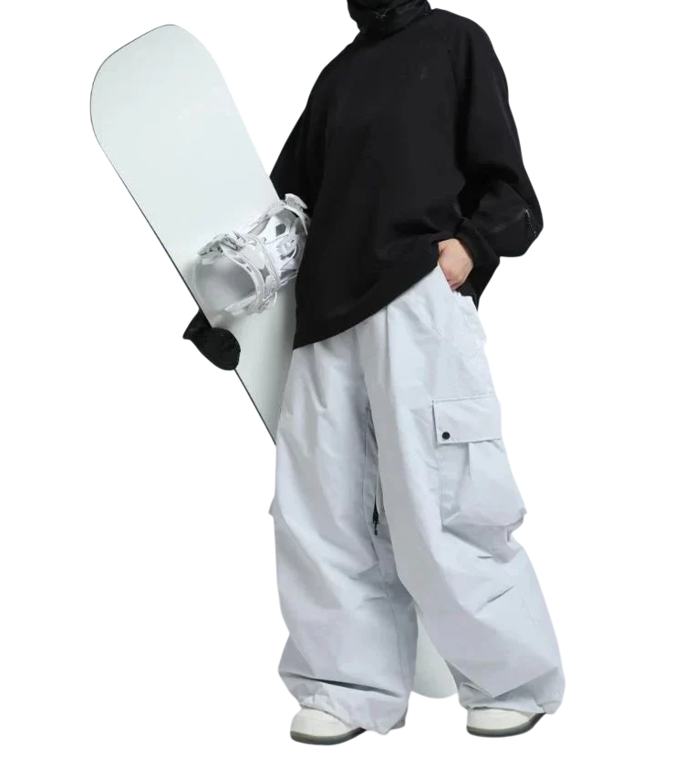 Osoba w odblaskowych goglach narciarskich, czarnym topie i Arkadya Outlet spodnie zimowe męskie szeroki krój regularny na warunki zimowe trzyma białą deskę snowboardową na jednolitym tle.