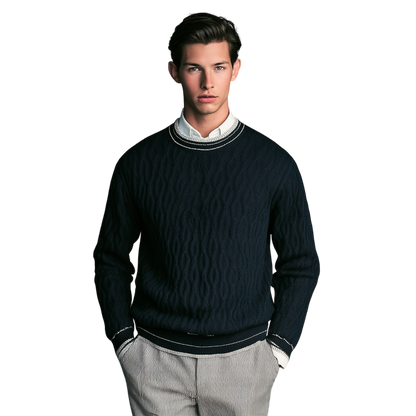 Młody mężczyzna o ciemnych włosach nosi lamówkę Arkadya Outlet Sweter męski dekolt okrągły kontrastowa lamówka na białej koszuli z kołnierzykiem i jasnych spodniach, stojąc z rękami w kieszeniach na prostym białym tle.