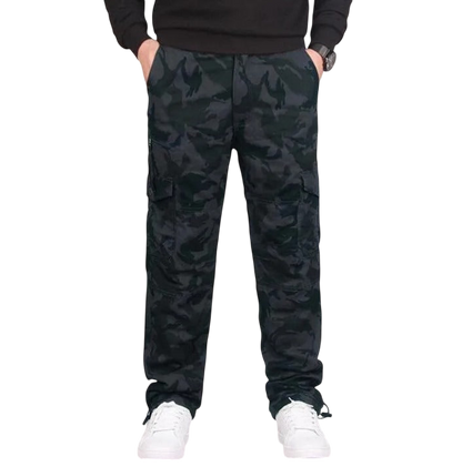 Mężczyzna ubrany w Arkadya Outlet Spodnie cargo męskie prosta nogawka z kieszeniami i zamkiem, czarną koszulę z długim rękawem i białe trampki stoi z rękami w kieszeniach na jednolitym tle.