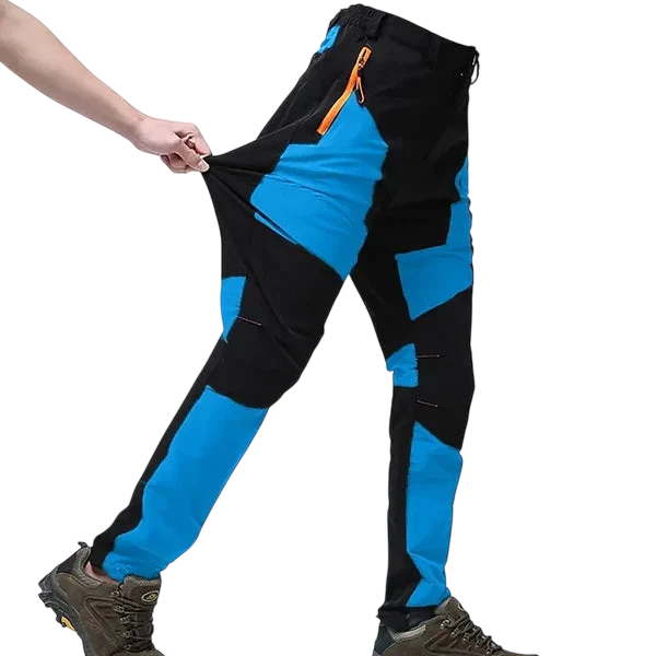 Osoba ubrana w Arkadya Outlet Spodnie Terenowe Męskie Wodoodporne Wiatroszczelne Regulowane i brązowe buty turystyczne rozciąga bok spodni, aby zademonstrować ich elastyczność na zwykłym białym tle.