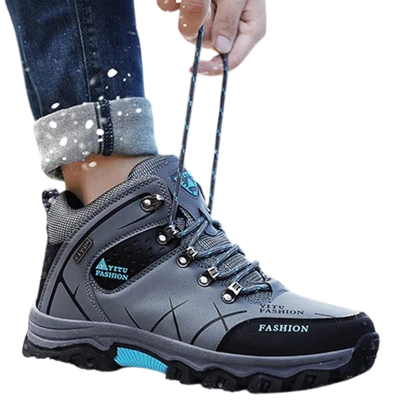 Osoba w podwiniętych dżinsach zawiązuje sznurówki szaro-czarnych butów Męskie Arkadya Outlet wodoodporna konstrukcja ergonomiczna podeszwa, stojąc na zewnątrz w padającym śniegu - idealne buty do codziennego użytkowania.