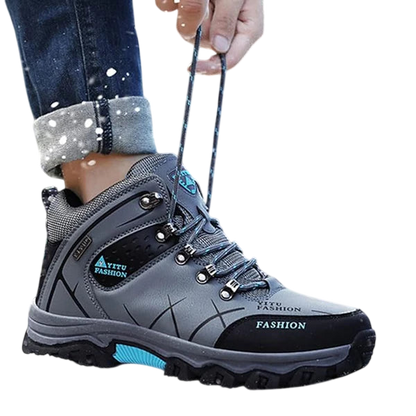 Osoba w podwiniętych dżinsach zawiązuje sznurówki szaro-czarnych butów Męskie Arkadya Outlet wodoodporna konstrukcja ergonomiczna podeszwa, stojąc na zewnątrz w padającym śniegu - idealne buty do codziennego użytkowania.