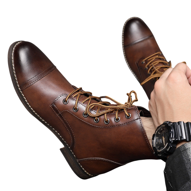 Mężczyzna w Arkadii Outlet Buty męskie wysoka cholewka z wiązaniem pełna wysokość i czarny zegarek siedzi na szarej podłodze wyłożonej kafelkami, jedna noga w butach skrzyżowana na drugiej.