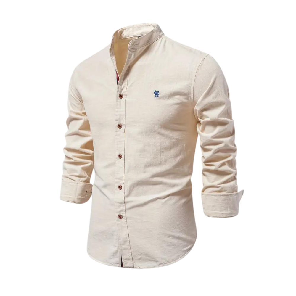 The Arkadya Outlet Koszula męska kołnierz stójka długi rękaw, krój regularny, w beżowym kolorze z niebieskim haftowanym logo na piersi. Idealna do codziennego użytku, prezentowana na manekinie na tle rozmytego wnętrza.