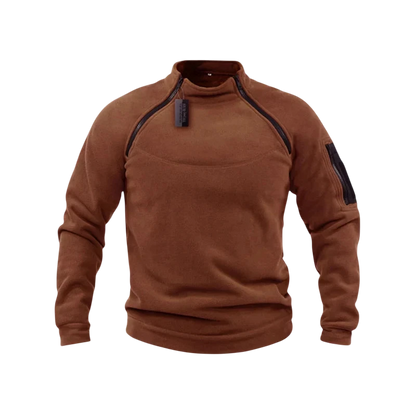 Arkadya Outlet Bluza męska polarowa długi rękaw z kieszeniami jest prezentowana w kolorze brązowym z zapinanym na zamek kołnierzem i kieszenią na rękawie, na rozmytym tle ośnieżonych gór.