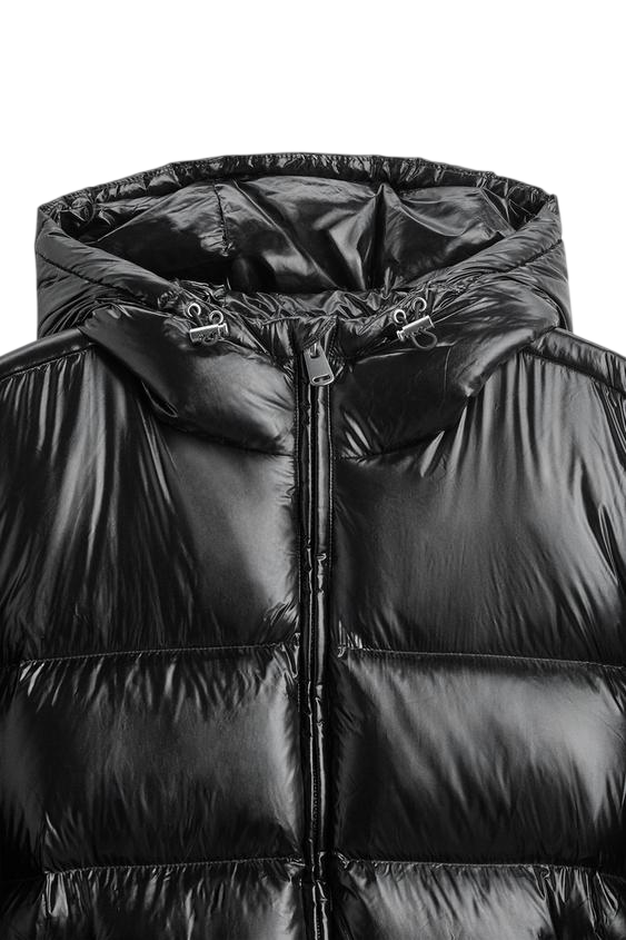 Zbliżenie na kurtkę Arkadya Outlet Kurtka Pikowana Męska Krótka Długość Konstrukcja Komorowa w błyszczącym czarnym kolorze, z kapturem, zamkiem z przodu i regulowanymi sznurkami do ściągania kaptura, pokazana na białym tle.