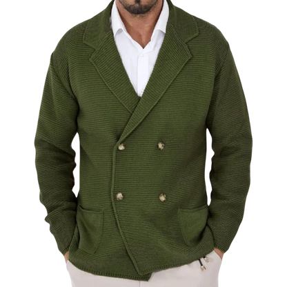 Mężczyzna w Arkadya Outlet Męski Kardigan, oliwkowozielonej dwurzędowej marynarce z kołnierzykiem, na białej koszuli i jasnych spodniach w pomieszczeniu, wieszaki na płaszcze rozmazane w tle.