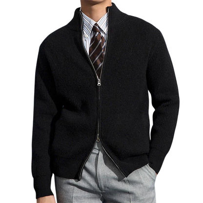 Przed ciemnoniebieską ścianą ozdobioną mapami stoi mężczyzna ubrany w kurtkę Męski Outlet Zapinany Na Zamek Błyskawiczny Dopasowany Krój, koszulę w paski i brązowy krawat oraz jasnoszare spodnie.