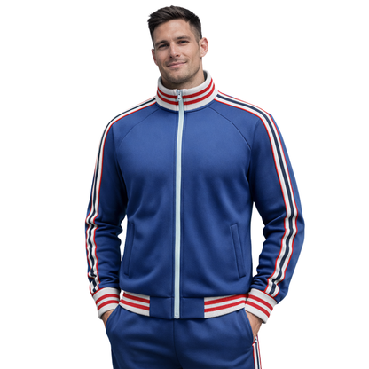 Uśmiechnięty mężczyzna w niebieskiej kurtce Arkadya Outlet Komplet dresowy męski dwuczęściowy zestaw do codziennego użytku i dopasowanych spodniach w biało-czerwone paski, pozuje z rękami w kieszeniach na białym tle.