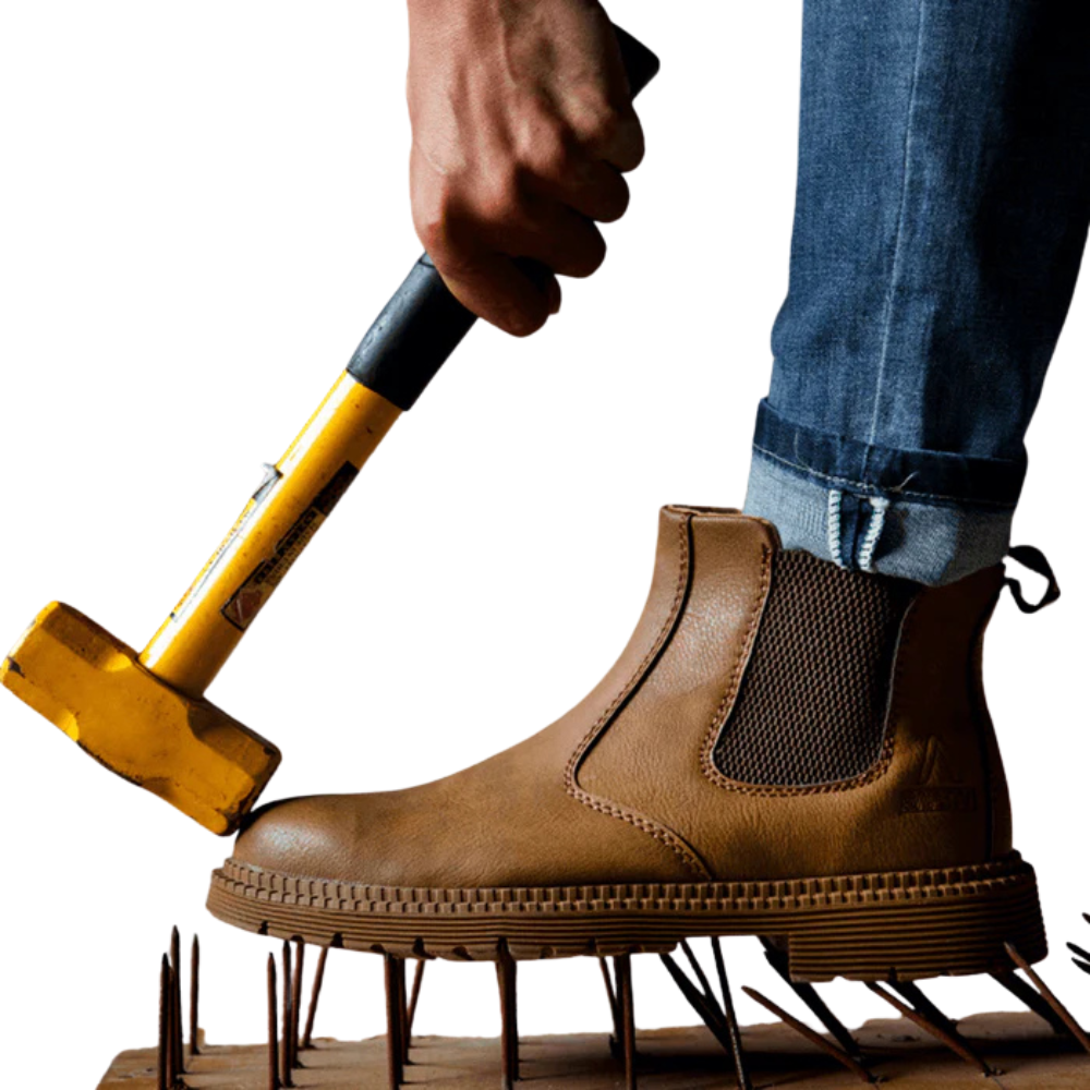 Ręka uderza w brązowy Arkadya Outlet Buty Robocze Męskie Zabudowany Nosek Trwała Konstrukcja żółtym młotkiem, noszonym przez kogoś stojącego na ostrych gwoździach, podkreślając ich wytrzymałość i ochronę. Białe tło.