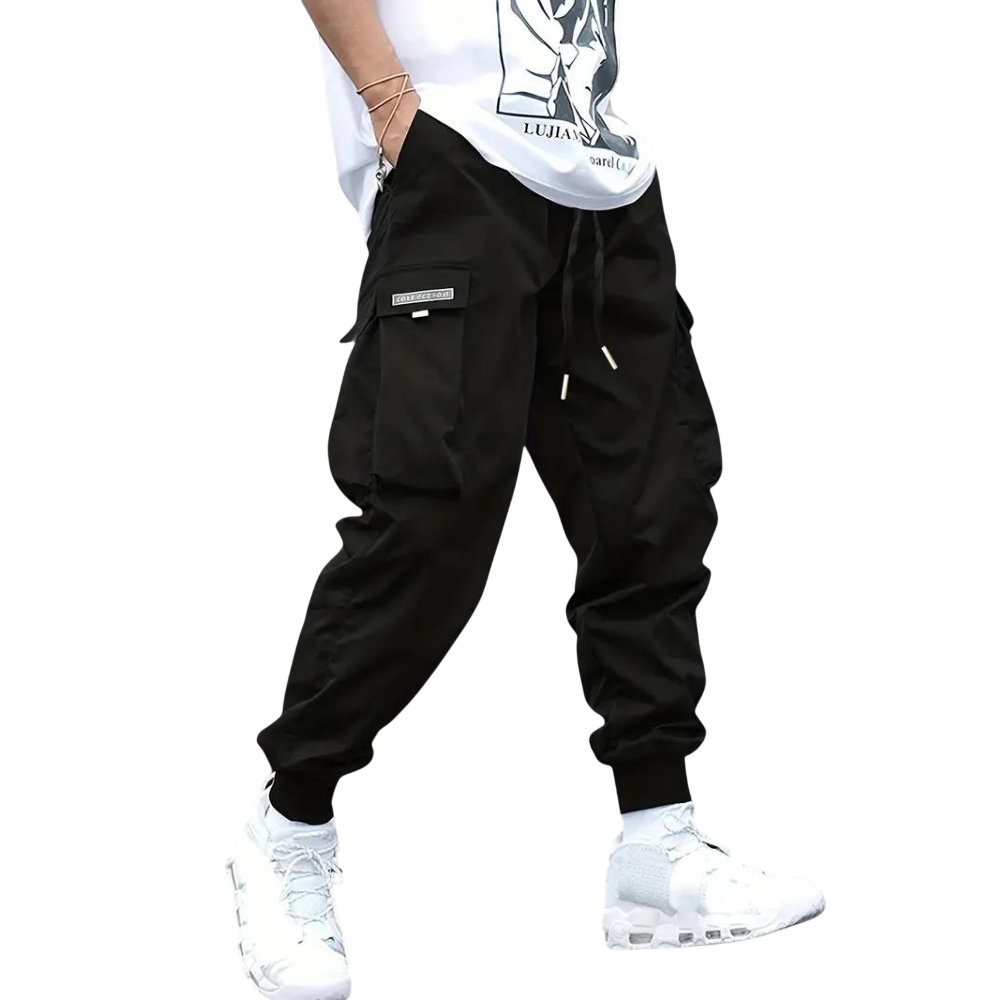 Osoba, widoczna od pasa w dół, nosi spodnie cargo Arkadya Outlet Męskie z wąską nogawką i wieloma kieszeniami, w połączeniu z białą koszulką z grafiką i białymi trampkami, stojąc na prostym szarym tle.