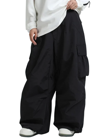 Osoba ubrana w oversizową białą koszulę z długim rękawem i Arkadya Outlet Spodnie zimowe męskie szeroki krój regularny na warunki zimowe, stojąca na jednolitym jasnym tle. Widoczna jest tylko dolna część ciała.