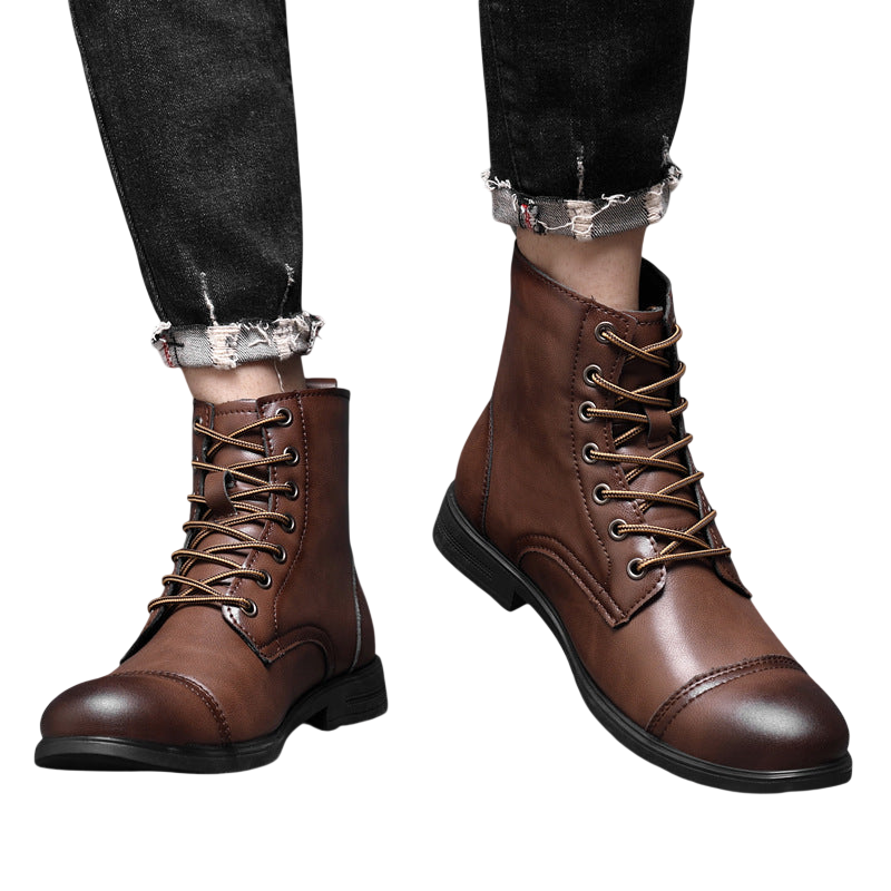 Osoba ubrana w Arkadya Outlet Buty męskie wysoka cholewka z wiązaniem pełna wysokość, brązowe skórzane sznurowane buty z czarnymi podeszwami, sparowane z czarnymi podartymi dżinsami, stojąca na podłodze wyłożonej kafelkami na tle szarej ściany.