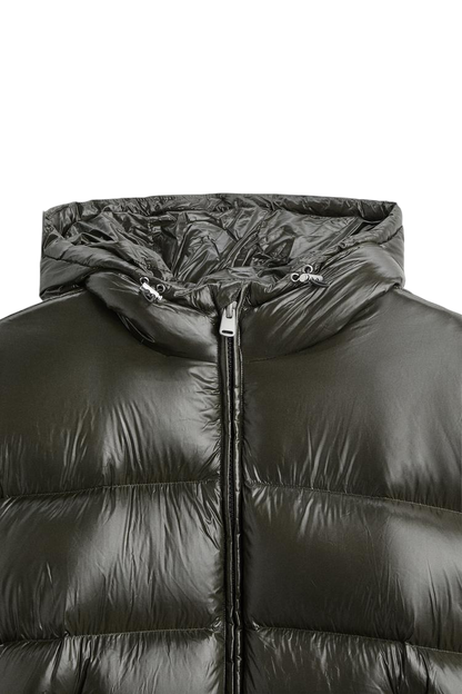 Zbliżenie na kurtkę Arkadya Outlet Pikowana Męska Krótka, z ciemnozielonym błyszczącym materiałem, kapturem ze sznurkiem ściągającym, zamkiem błyskawicznym z przodu i poziomym pikowaniem komorowym.