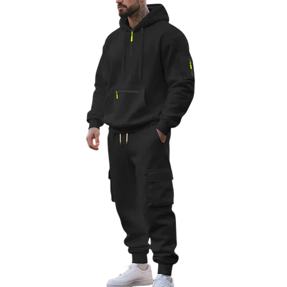 Mężczyzna nosi Arkadya Outlet Męski dres wyściełane wnętrze dwuczęściowy komplet z zamkiem z żółtymi akcentami, stojąc na parkowej ścieżce we wczesnym porannym słońcu, otoczony drzewami i trawą.