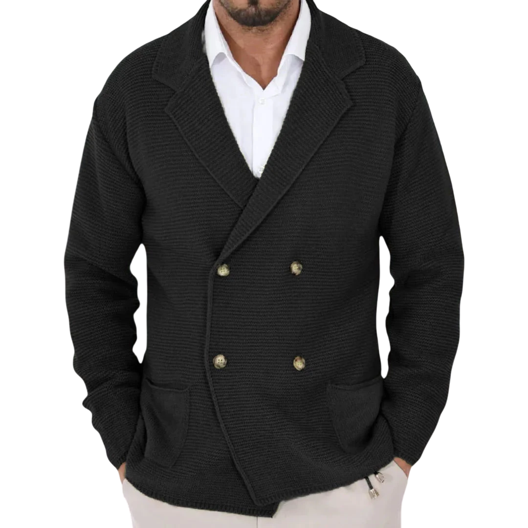 Mężczyzna stoi z rękami w kieszeniach, ubrany w Arkadya Outlet Męski Kardigan o dwurzędowym kroju typu marynarka z kołnierzem na białej koszuli w delikatnym, nowoczesnym wnętrzu.