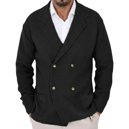 Mężczyzna stoi z rękami w kieszeniach, ubrany w Arkadya Outlet Męski Kardigan o dwurzędowym kroju typu marynarka z kołnierzem na białej koszuli w delikatnym, nowoczesnym wnętrzu.