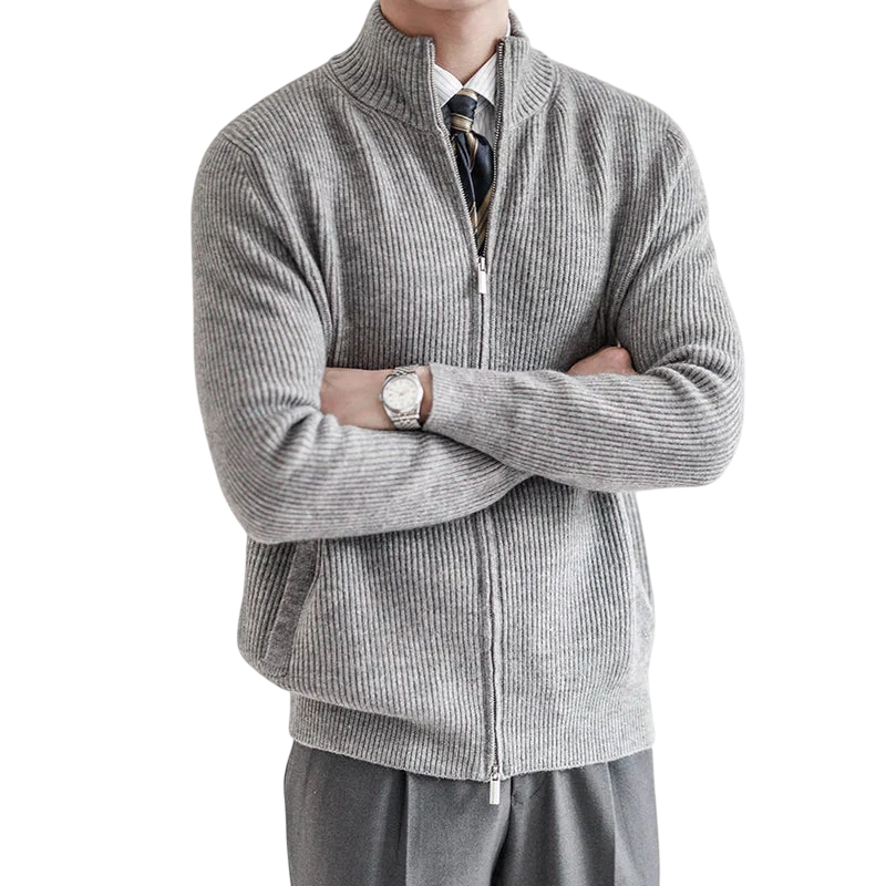 Mężczyzna stoi ze skrzyżowanymi rękami w jasnoszarym Arkadya Outlet Męski kardigan, zapinany na zamek błyskawiczny i o dopasowanym kroju. Ubrany w białą koszulę, krawat w paski i szare spodnie; twarz zasłonięta. Tło neutralne, delikatnie oświetlone.