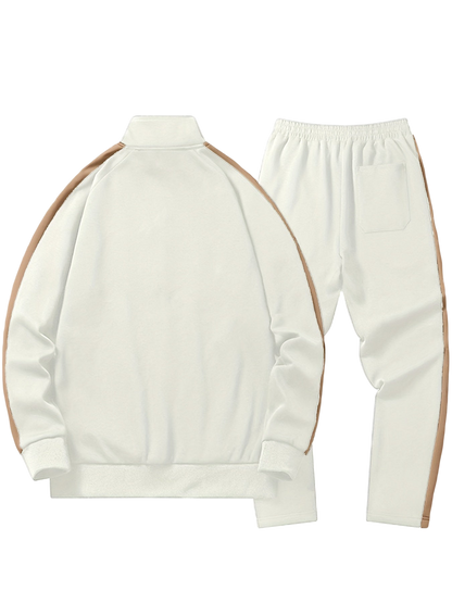 Arkadya Outlet Komplet dresowy męski dwuczęściowy codzienny strój w kolorze kremowym z zapinaną na zamek kurtką i dopasowanymi spodniami w jasnobrązowe paski, elastycznym paskiem w talii i tylną kieszenią, pokazany na płasko na białym tle.