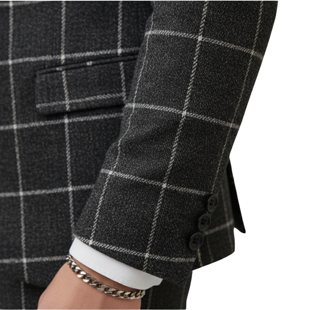 Zbliżenie na ramię osoby ubranej w ciemnoszarą koszulkę Arkadya Outlet Komplet Garniturowy Męski Trzyczęściowy Marynarka w białą kratkę, z mankietem białej koszuli, czarnymi guzikami na rękawach i srebrną bransoletką na łańcuszku na nadgarstku.